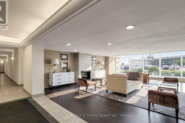 Lobby seating area with a fireplace, white dresser, and large windows overlooking the parking lot. - 310 - 7811 Yonge Street, Markham