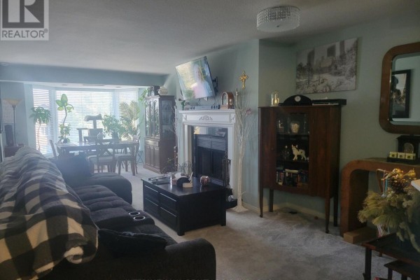 Apartment living room with a fireplace, dark sofa, and a dining area by bay windows. - 310 - 85 Wellington Street W, Aurora