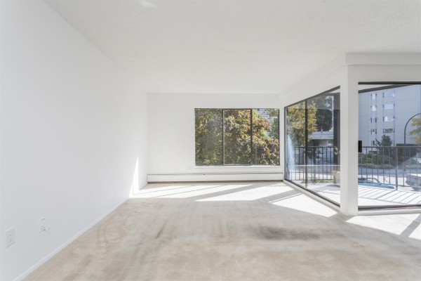 Empty living room with beige carpet, white walls, and large windows. - 310 1437 Foster Street, White Rock