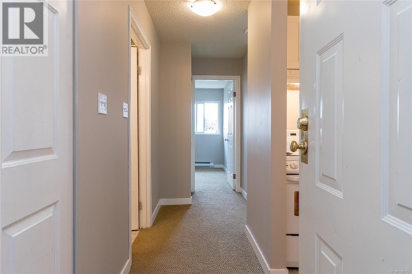 Hallway inside the apartment with beige carpet and doors opening to rooms. - 310 2515 Alexander St, Duncan