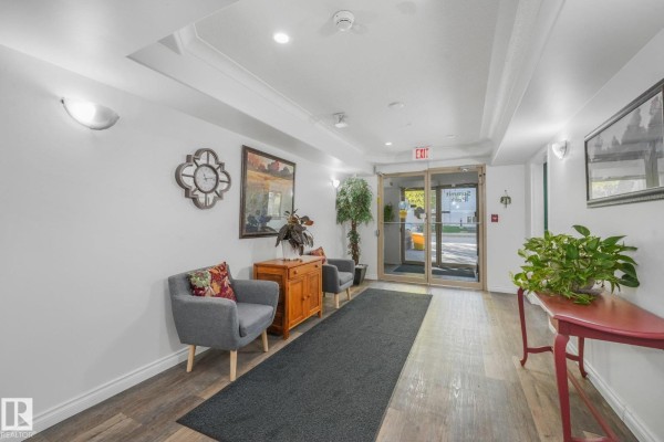 Apartment building lobby with grey chairs, wooden cabinet, artwork, and plants. - #310 4806 48 Av, Leduc
