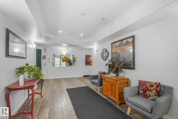 Hallway view of the apartment lobby with two grey chairs and a red table. - #310 4806 48 Av, Leduc