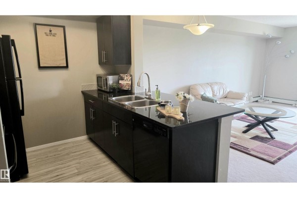 Black electric stove, dark wood cabinetry, and a black refrigerator in a galley kitchen layout. - #310 5370 Chappelle Rd Sw Sw, Edmonton