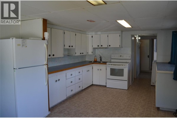 Kitchen with white cabinets, white appliances, a double sink, and beige tile flooring. - 310 Bancroft Street, Ashcroft