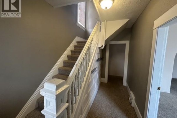 Interior staircase with beige carpet and white wooden banister, leading to the second floor. - 310 High Street W, Moose Jaw