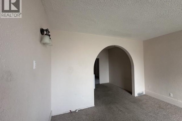 Living room with light beige walls, carpet, and an arched doorway to another room. - 310 High Street W, Moose Jaw