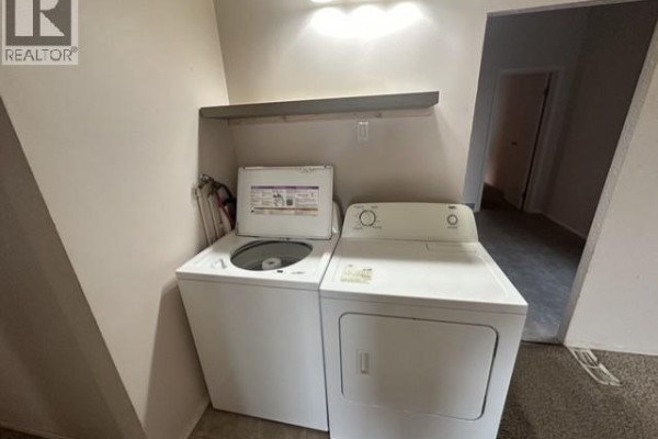 Laundry room with a white top-load washing machine and a white front-load dryer. - 310 High Street W, Moose Jaw