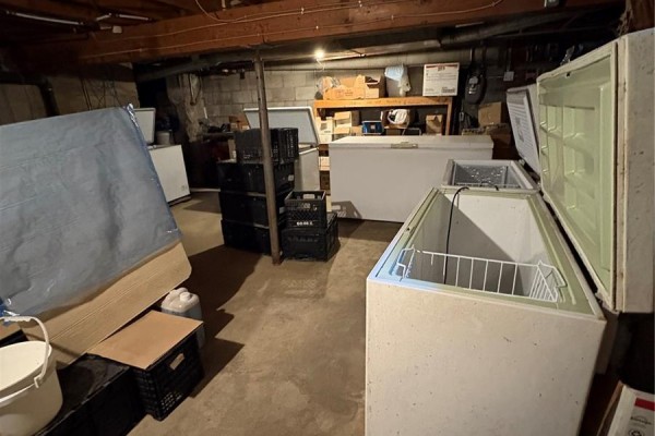 Basement storage area with multiple open chest freezers, stacked crates, and mattresses. - 310 Main Street N, Ituna