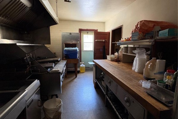 Commercial kitchen with stainless steel fryers, large prep table, and stainless steel hood. - 310 Main Street N, Ituna