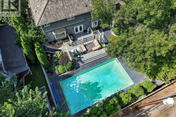 Aerial view of a house with a large rectangular swimming pool and a multi-level wooden deck. - 310 Saskatchewan Crescent W, Saskatoon