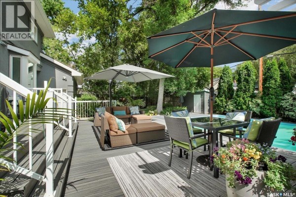 A grey wooden deck with outdoor seating, dining set, and a large swimming pool. - 310 Saskatchewan Crescent W, Saskatoon