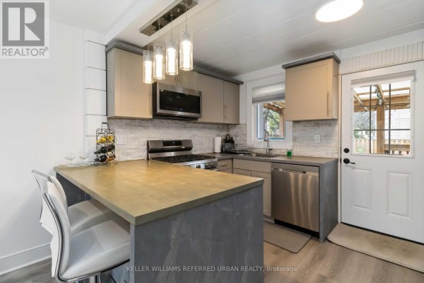 Kitchen with island seating, stainless steel dishwasher, and a door leading outside. - 310 Senlac Road, Toronto