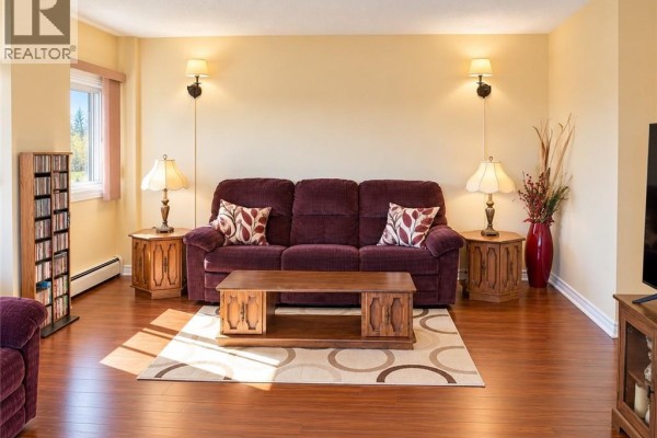 Living room with a burgundy sofa, wooden coffee table, and hardwood floors. - 310 Woodward Avenue Unit# 1114, Saint John