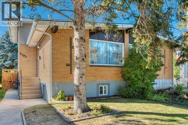Exterior view of a brick duplex with a sloped front yard and a large tree in front. - 3103a 38 Street Sw, Calgary