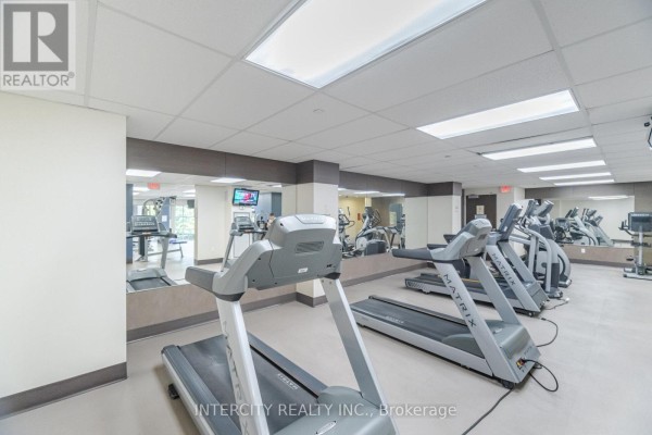 Gym with multiple treadmills, ellipticals, and weight machines, featuring mirrored walls and bright lighting. - 3104 - 23 Sheppard Avenue E, Toronto