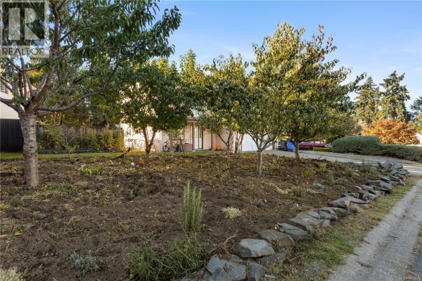 A garden area with freshly tilled soil, small trees, and a stone border in front of a house. - 3104 Laurel Grove, Duncan