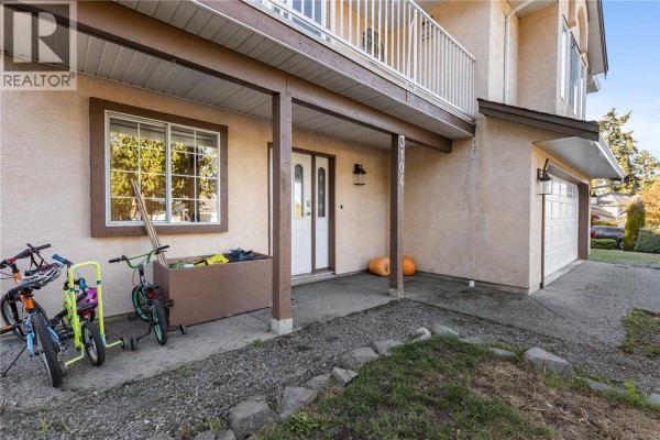 Close-up of the front entrance of a peach stucco house with a covered porch and a double garage. - 3104 Laurel Grove, Duncan