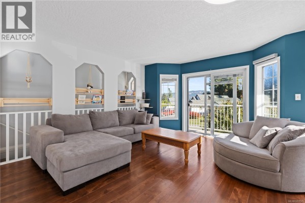 Living room with a sectional sofa, armchair, coffee table, and a sliding glass door to a balcony. - 3104 Laurel Grove, Duncan