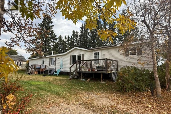 Exterior view of the rear of a mobile home with a wooden deck and surrounding trees and lawn. - 31040a Twp Rd 524, Rural Vermilion River, County Of