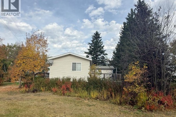 Side view of the mobile home with tan siding, surrounded by trees and shrubs in autumn foliage. - 31040a Twp Rd 524, Rural Vermilion River, County Of