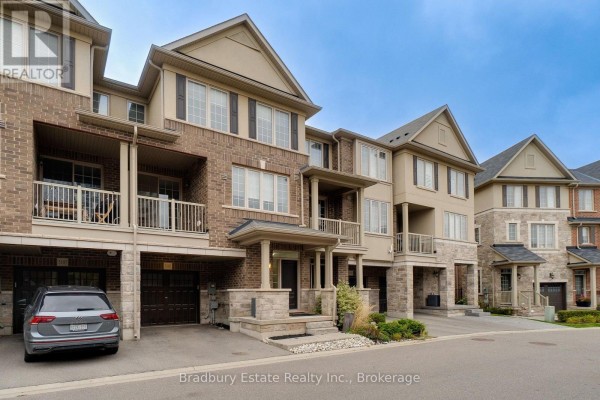 Side exterior view of a brick and beige townhouse with garages and balconies. - 3105 Blackfriar Common, Oakville