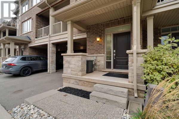 Covered front porch with stone pillars, dark door, and exterior light fixture. - 3105 Blackfriar Common, Oakville