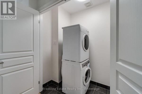 Compact laundry room with white stacked washer and dryer on dark tile flooring. - 3105 Blackfriar Common, Oakville