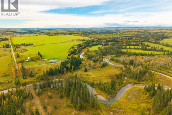 Aerial view of a meandering river bordered by fields and forest, with a farmstead visible on the left. - 31064 Range Road 52, Rural Mountain View County