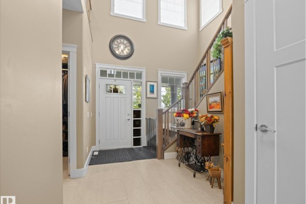 Foyer with a high ceiling, white front door, cream tiled floor, and wooden staircase. - 3107 Cameron Heights Wy Nw, Edmonton
