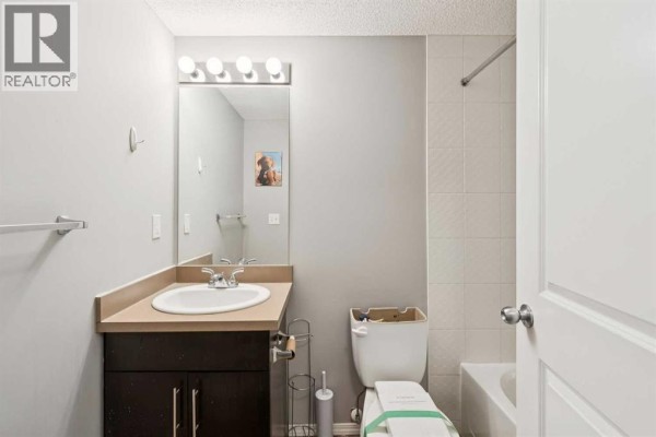 Bathroom vanity with light countertop, dark cabinet, sink, mirror, and bathtub. - 3108, 403 Mackenzie Way Sw, Airdrie