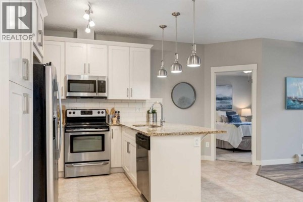 Kitchen with white cabinetry, stainless steel refrigerator, microwave, and stove. - 3109, 522 Cranford Drive Se, Calgary