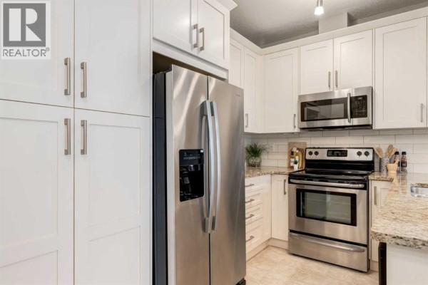 Kitchen island with sink and dishwasher, open to living room and hallway with beige tiled floor. - 3109, 522 Cranford Drive Se, Calgary