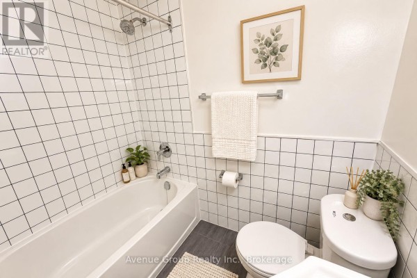 Bathroom with a white bathtub, toilet, white tiled shower walls, and a vanity. - 311 - 1053 Don Mils Road, Toronto