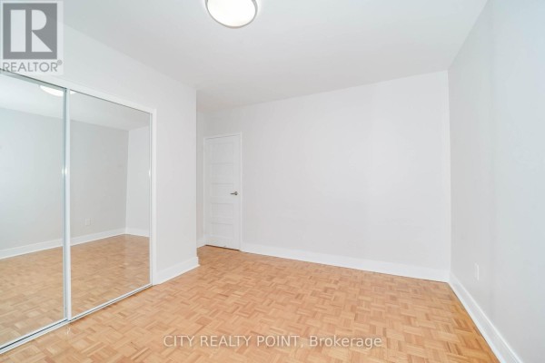 Empty room with light grey walls, parquet flooring, and a mirrored closet door. - 311 - 1291 Bayview Avenue N, Toronto