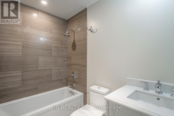 Bathroom featuring a white bathtub with wood-look tile accent wall and a white vanity with double sinks. - 311 - 1451 Wellington Street W, Ottawa