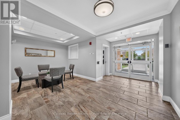 Building entrance lobby with grey walls, patterned chairs, a coffee table, and tile flooring. - 311 - 2 Colonial Drive, Guelph