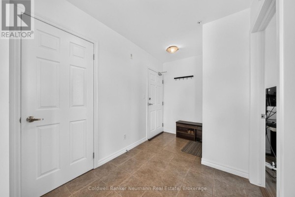 Apartment hallway with two white doors, tile flooring, and a small bench by the entrance. - 311 - 2 Colonial Drive, Guelph