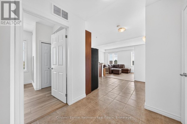 Interior view from the hallway into a living room with white walls and beige tile flooring. - 311 - 2 Colonial Drive, Guelph