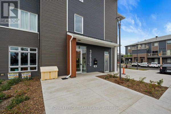 Another view of the building entrance and walkway, showing parking area on the right. - 311 - 3600 Brian Coburn Boulevard, Ottawa