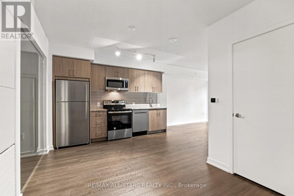 Modern kitchen with stainless steel appliances, wood cabinets, and granite countertops. - 311 - 4010 Eglinton Avenue W, Toronto