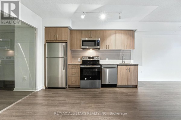 A modern condo kitchen with stainless steel appliances and wood cabinetry is shown. - 311 - 4010 Eglinton Avenue W, Toronto