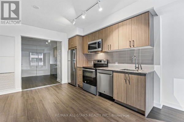 Kitchen area featuring stainless steel appliances, wood cabinets, and a view into another room. - 311 - 4010 Eglinton Avenue W, Toronto