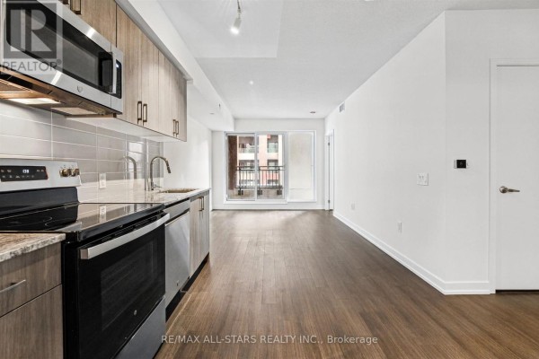 Kitchen with stainless steel appliances, wood cabinets, and a view of a balcony and living area. - 311 - 4010 Eglinton Avenue W, Toronto
