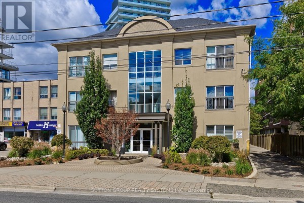 Side view of a beige stucco building exterior with trees and landscaping. - 311 - 4198 Dundas Street W, Toronto