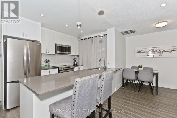 Modern kitchen with white cabinets, stainless steel appliances, and island with bar stools. - 311 - 4198 Dundas Street W, Toronto