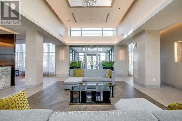 Modern lobby seating area with a sectional sofa, glass coffee table, and marble reception desk. - 311 - 4633 Glen Erin Drive, Mississauga