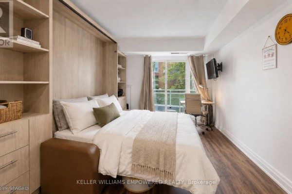 Living space with a murphy bed pulled down, wood shelving, and a desk by the window. - 311 - 8 Scollard Street, Toronto