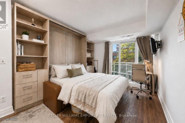 Bedroom with a murphy bed, built-in shelving, a desk, and a view of trees outside. - 311 - 8 Scollard Street, Toronto