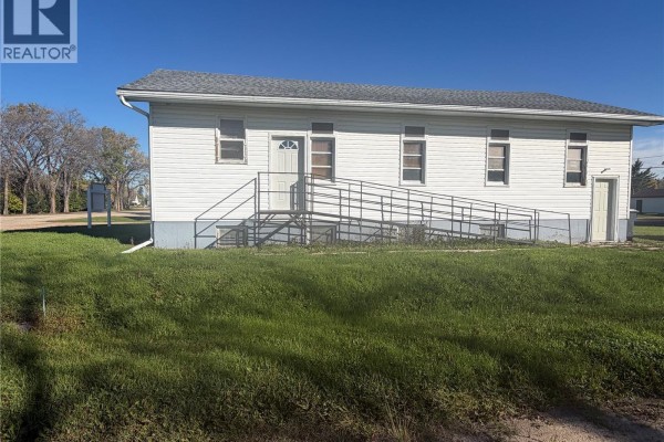 Front exterior of a white vinyl sided building with windows, a ramp, and a side door. - 311 & 208 Main Street, Pelly