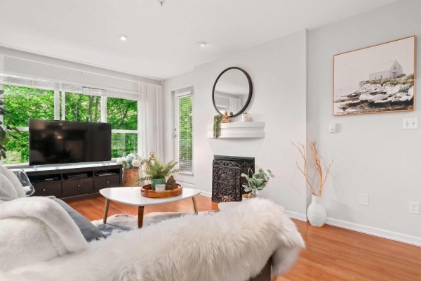 Living room with sofa, large TV, decorative fireplace, mirror on shelf, and artwork on wall. - 311 10188 155 Street, Surrey
